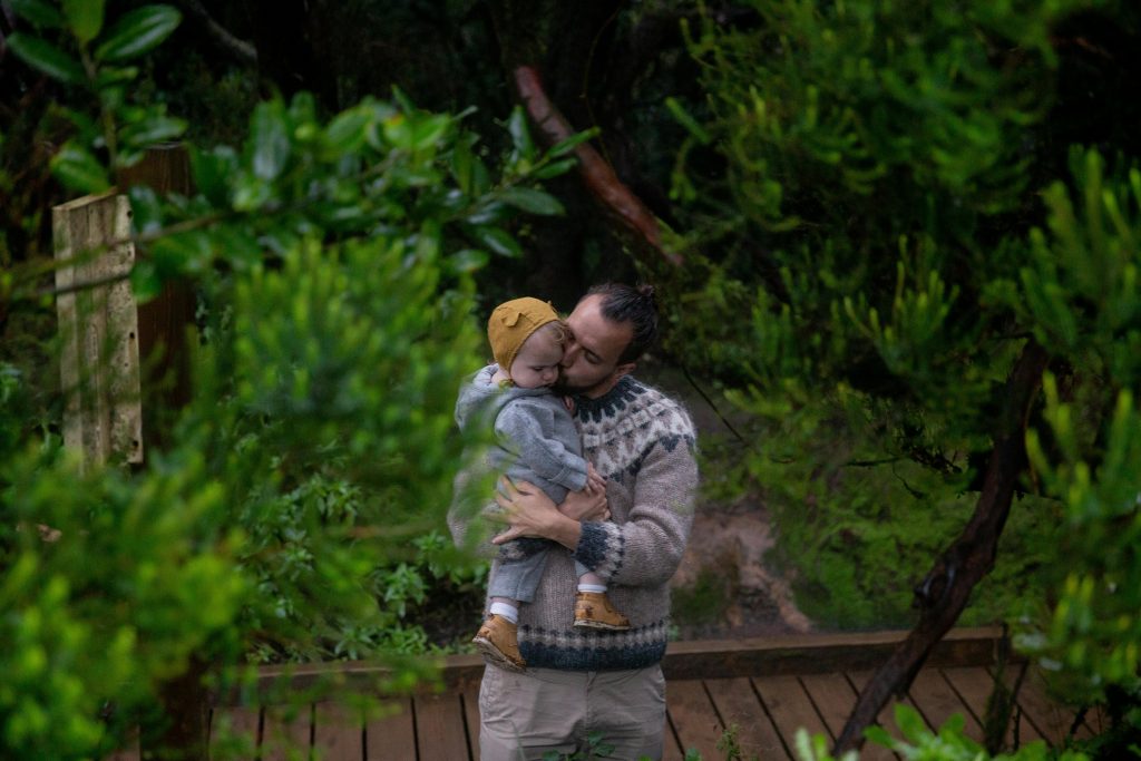 From above middle age dad holding on hands and kissing small kid in green forest